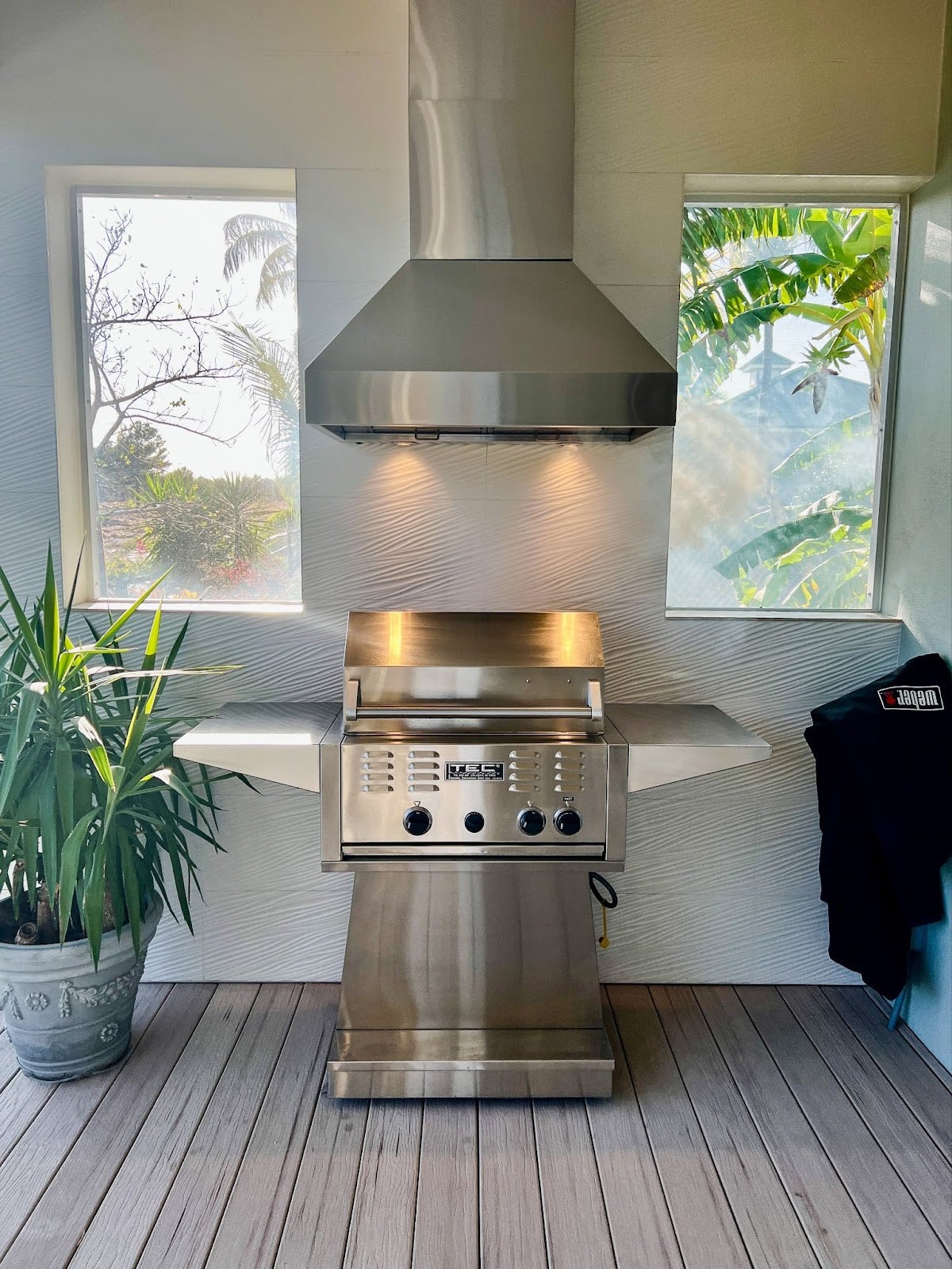 Sleek and minimalistic outdoor kitchen with a powerful range hood, set against a backdrop of modern landscaping and ambient lighting -prolinerangehoods.com.